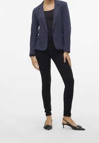 Mörkblå kavaj i texturerat tyg, kombinerad med en svart topp och svarta smala jeans. Skorna består av svarta slingbackklackar med rosett. 