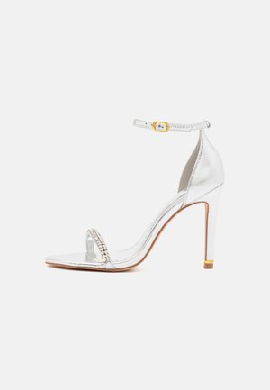 Silver high-heeled sandal with a thin ankle strap, embellished with rhinestones across the toe, and a leather-like texture.
