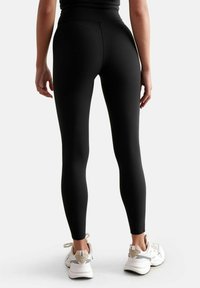 Leggings fitness neri con vita alta, design aderente e texture liscia, abbinati a scarpe da ginnastica bianche.