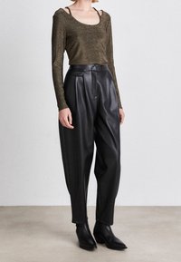 Långärmad, kort topp i mörk, metallisk tyg som matchas med högmidjade, svarta läderbyxor och spetsiga svarta ankelstövlar.