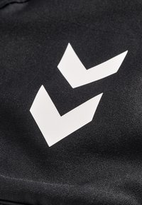 Zwarte stof met twee witte geometrische vormen die op chevrons lijken, met een gestructureerde uitstraling. Het ontwerp is gedurfd en modern.