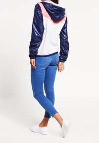 Färgblockerad vindjacka i marinblått, rosa och vitt, med huva och elastiska mudd, matchad med slimfit blå jeans och vita sneakers.