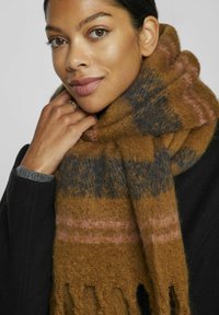 Brun og grå mønstret tørklæde lavet af blødt materiale, med frynser i enderne og en subtil lyserød stribe. Båret om halsen.