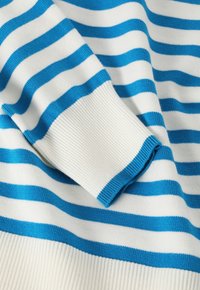 Weißer Pullover mit kräftigen blauen horizontalen Streifen; verfügt über gerippte Bündchen und eine weiche, gestrickte Textur. Die Streifen variieren in der Breite.