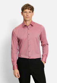 Long-sleeve, fitted red checkered shirt with a spread collar and button front. Features dark buttons and cuff accents. Paired with black trousers.