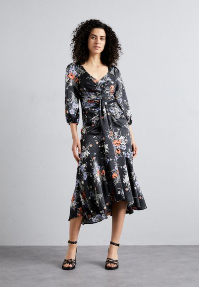 Schwarzes Blumenkleid mit drei Viertelärmeln, gerafftem Oberteil und ausgestelltem Saum. Verziert mit mehrfarbigen Blumen und einer glatten Stoffstruktur. Schwarze Riemchen-Heels.