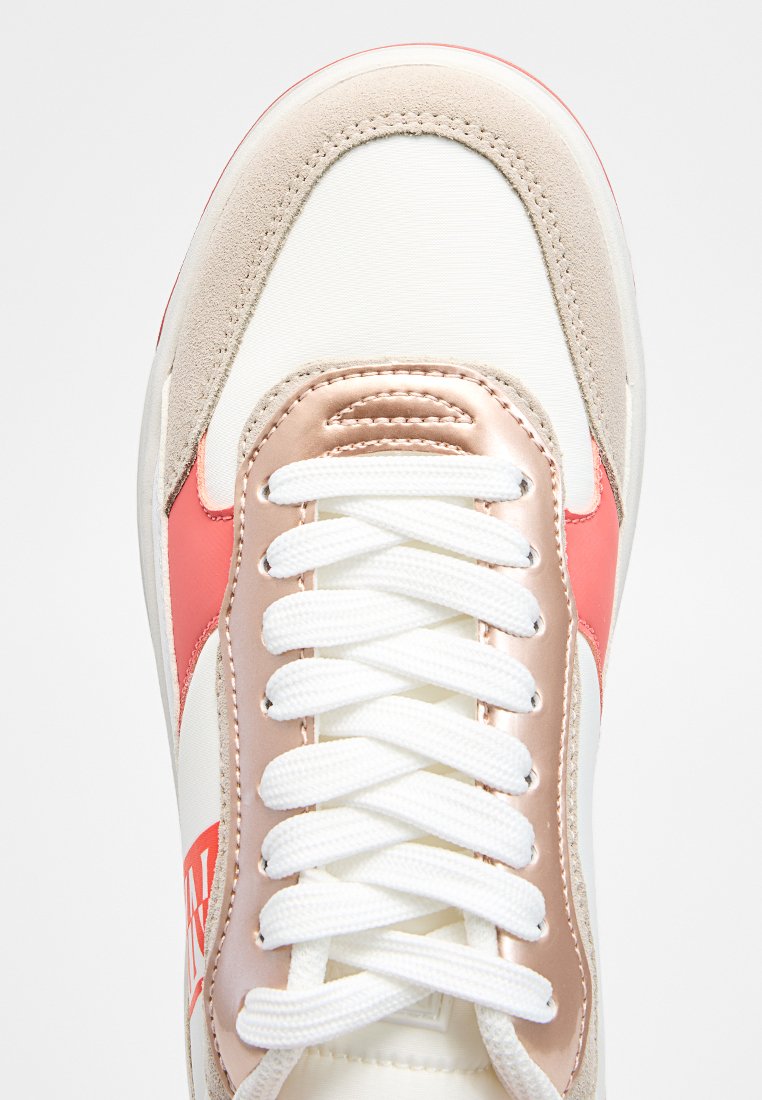 Zapatilla blanca y beige con panel de ojales metálicos en oro rosa, cordones blancos y detalles en coral, vista desde arriba.