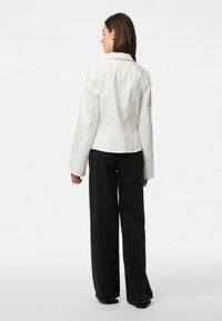 Giacca bianca con un design aderente e maniche larghe, abbinata a pantaloni neri a gamba larga, che mostrano una texture liscia e linee pulite.