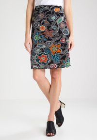 Jupe brodée florale en tissu noir avec des fleurs et des feuilles colorées, longueur genou, ourlet festonné. Associée à des mules noires.