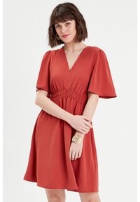 Vestido de color óxido con escote en V, mangas cortas abullonadas, cintura elástica y falda acampanada. Tejido suave y ligero con una textura sutil.