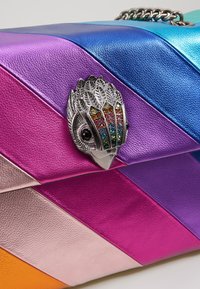 Multikleur leren tas met diagonale strepen in roze, paars en blauw. Voorzien van een zilveren vogelvormige sluiting met meerkleurige versieringen.