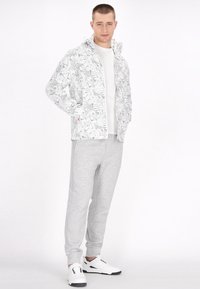 Let vest, hvid jakke med grå bladmønster, parret med grå sweatpants og hvide sneakers. Outfittet har lommer og hætte.