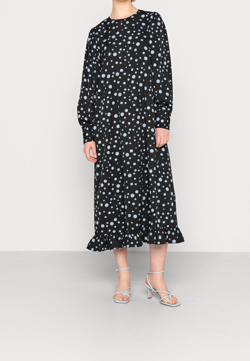 Černé šaty s dlouhým rukávem, které mají světle modré puntíky, volánkový lem a volný střih. V kombinaci se světle modrými sandály na podpatku.