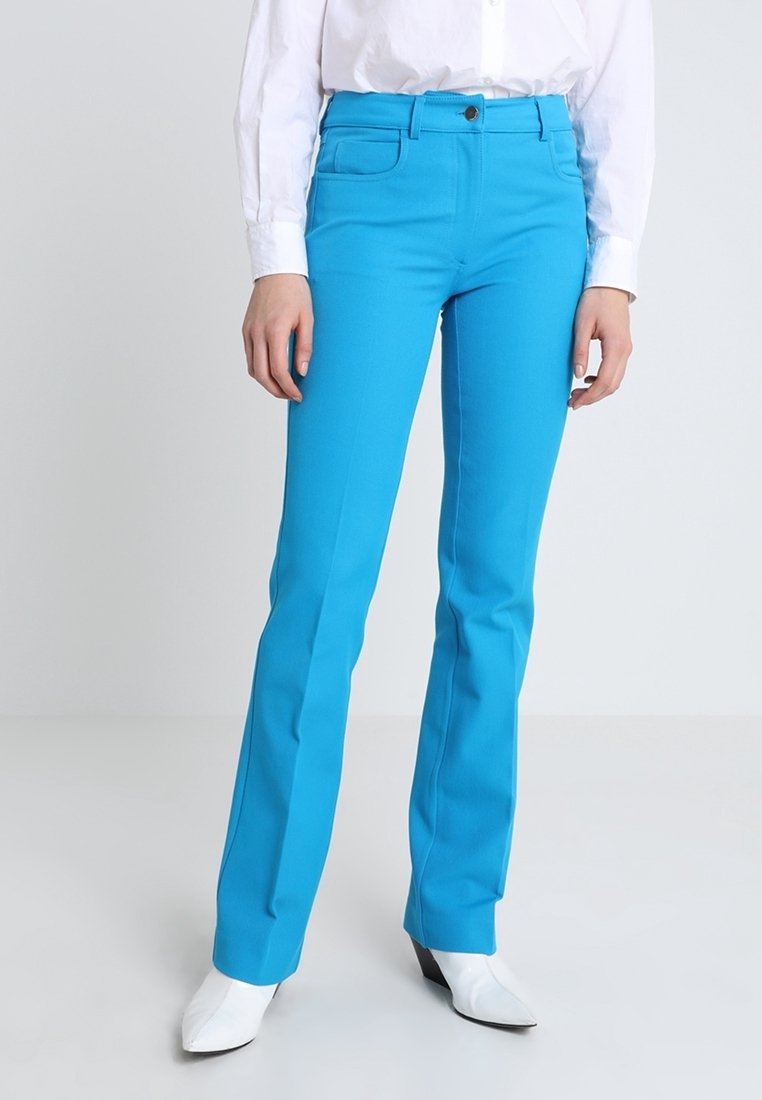 Pantalons slim-fit bleu vif avec une texture lisse, dotés de deux poches avant et d'une ceinture simple, associés à des chaussures blanches pointues.