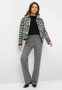 Giacca in pile con stampa leopardata bianca e nera, design con colletto, chiusura con zip, abbinata a pantaloni grigi e stivali neri con tacco.