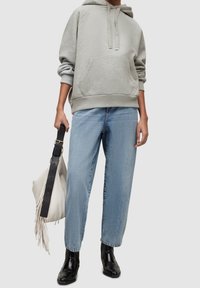 Felpa grigia con cappuccio e tasca frontale, abbinata a jeans a gamba dritta azzurri e stivaletti neri alla caviglia. La modella tiene una borsa bianca.