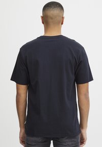 Tricou scurt cu mânecă din bumbac, de culoare albastru închis, cu guler rotund și o croială confortabilă. Vederea din spate arată o textură netedă, fără grafică.