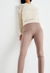 Gräddfärgad stickad tröja med öppet mönster och långa ärmar, kombinerad med figurnära nudefärgade leggings med sömdetaljer längs sidorna.