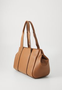 Bruine leren totebag met twee lange handvatten, een gestructureerd maar zacht vorm. Heeft een textuur oppervlak, minimale stiksels en gouden hardware.