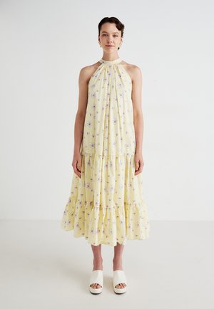 Yellow floral midi dress with a halter neck, gathered design, and ruffled hem. Model paired it with white platform shoes.