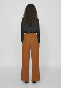 Black long-sleeve blouse with a smooth texture paired with high-waisted, wide-leg, rust-colored pants featuring a gathered waistband.