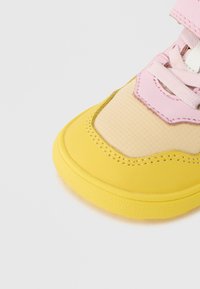 Κίτρινο αθλητικό παπούτσι με ροζ λεπτομέρειες, με υφασμένο άνω μέρος με υφή, στρογγυλεμένη μύτη, λαστιχένια σόλα και αντίθετες ραφές.