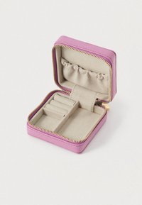 Kompaktní růžová šperkovnice s béžovým měkkým interiérem, přihrádky na prsteny, elastická kapsa a zlatý zip částečně rozepnutý na bílé pozadí.