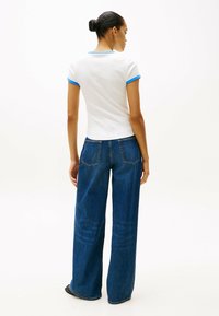 Camiseta blanca con ribete azul, combinada con unos vaqueros de mezclilla azul de corte holgado. El tejido parece suave, con un diseño sencillo y un ajuste informal.