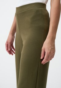 Olivengrüne, hoch sitzende Hosen aus weichem Stoff, mit einer figurbetonten Passform und seitlichen Taschen, die eine glatte Textur und eine weite Beinsilhouette aufweisen.