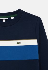 Felpa navy con strisce orizzontali in blu, bianco e oliva, con una superficie testurizzata. Logo Lacoste ricamato sul petto.