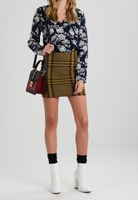 Hedvábná blůza s dlouhým rukávem v námořnické modré barvě s květinovým vzorem spárovaná s mini sukní v hořčicovém kostičkovaném vzoru. Bílá kotníková obuv, černé ponožky a mnohobarevná kabelka dotvářejí celkový vzhled.