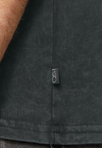 Zwarte katoen T-shirt met ribbelstructuur, voorzien van een klein merkembleem op de zijnaad. Stiksels zichtbaar bij de zoom.