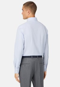 Camicia a righe blu chiaro e bianca con bottoni, maniche lunghe, yoke posteriore e polsini a tamburo, abbinata a pantaloni grigi e una cintura intrecciata.