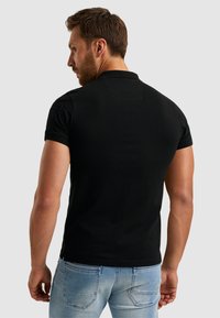 Polo shirt noir à manches courtes au design uni, avec un col et des détails brodés aux épaules, porté avec un jean bleu clair.