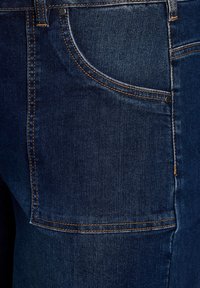 Tejido de mezclilla azul oscuro con costuras visibles, que presenta un bolsillo frontal y un bolsillo trasero. Textura suave con marcas de desgaste mínimas.