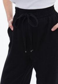 Pantaloni neri con cintura arricciata, lacci e tasche laterali. Morbido al tatto e vestibilità rilassata, adatti per un abbigliamento casual.