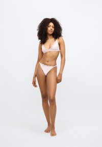 Set de lenjerie intimă din dantelă roz deschis, format dintr-un bralette cu bretele ajustabile și un tanga cu talie joasă, cu margini din dantelă și accente cu buline.