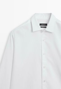 Weißes Langarmshirt mit Standardkragen, ausgestattet mit einer Knopfleiste vorne und einer glatten Stoffoberfläche. Markenetikett innen am Kragen sichtbar.