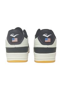 Le sneakers in bianco e nero presentano un design testurizzato, suola in gomma e tacco rialzato. Gli accenti comprendono un logo e una piccola bandiera americana sul tallone.