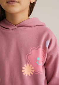 Rózsaszín kapucnis pulóver virág- és nap grafikával, sima textúrával és klasszikus dizájnnal. A díszítések pasztellszínekben vannak.