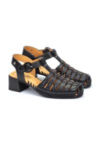 Sandalias de cuero negro con punta abierta, diseño en forma de cruz, tacón bajo y correa ajustable con costura decorativa y acentos metálicos.