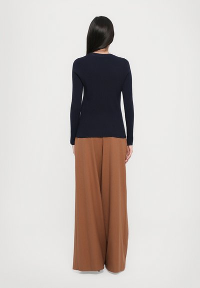Navy ribbed long-sleeve top paired with wide-legged brown trousers. Smooth fabric texture with a fitted silhouette and crew neck design.