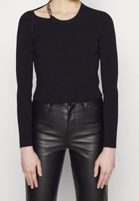 Haut long à côtes noir avec une découpe unique sur l'épaule, associé à un pantalon en cuir noir ajusté, mettant en valeur une texture lisse et élégante.