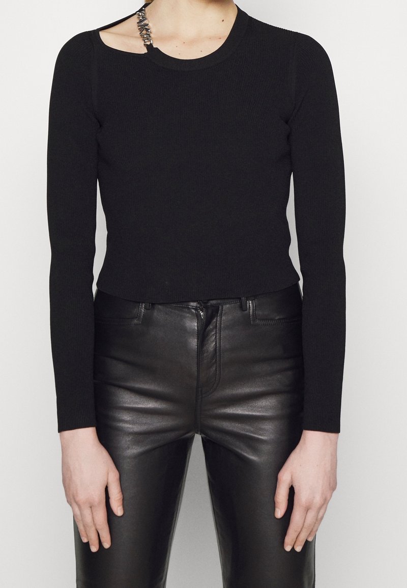 Haut long à côtes noir avec une découpe unique sur l'épaule, associé à un pantalon en cuir noir ajusté, mettant en valeur une texture lisse et élégante.