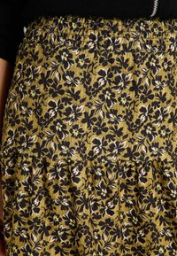 Falda floral en verde oliva con estampado floral en negro y crema. Presenta una cinturilla fruncida y detalle de volantes en capas en la parte inferior.