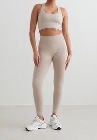 Soutien-gorge de sport beige côtelé et leggings taille haute en tissu doux et extensible, associés à des chaussures de sport blanches. Design simple et fonctionnel.