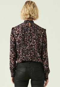 Bluzka z poliestru z kwiatowym wzorem w czerni, czerwieni i bieli, z wysokim kołnierzem, falbankami i wycięciem na plecach.