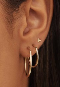 Gouden ring oorbellen en een kleine gouden stud, die een gladde metalen afwerking tonen. De ringen zijn gelaagd en hebben een gepolijste textuur.