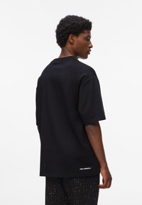 Černé oversized tričko s krátkými rukávy a kulatým výstřihem, s logem na lemu, vyrobené z hladké bavlněné látky.