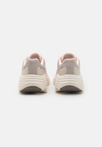 Light beige sneakers with textured mesh upper, soft pink accents around the collar, and a thick, ridged white sole.
